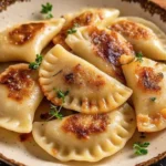Golden, pan-fried Polish meat pierogi topped with caramelized onions and served with sour cream and fresh dill on a rustic plate.