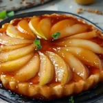 A beautifully caramelized pear tarte tatin on a rustic wooden table with a slice cut out