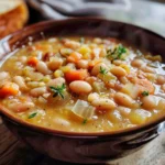 A bowl of navy bean soup topped with fresh parsley and served with crusty bread