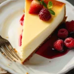 A slice of creamy New York cheesecake topped with fresh strawberries and whipped cream on a white plate