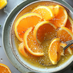 A vibrant orange vinaigrette in a glass jar with fresh oranges and herbs