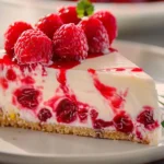A slice of raspberry bake cheesecake topped with fresh raspberries and mint leaves on a white plate.
