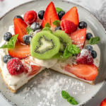 A vibrant watermelon fruit pizza topped with ricotta cheese, mint leaves, and colorful fruits on a wooden platter