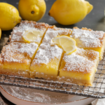 Plate of freshly baked lemon squares dusted with powdered sugar, garnished with lemon slices and mint leaves