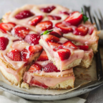 Delicious strawberry lemon blondies topped with fresh strawberries and lemon zest on a wooden cutting board.